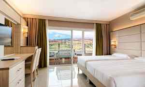 Hotellrom med to enkeltsenger, skrivebord og utsikt mot landskap gjennom en glassdør. (AI-generert tekst)