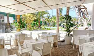 Utendørsrestaurant med hvite bord og stoler, samt utsikt over en frodig hage. (AI-generert tekst)