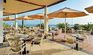 Restaurant med uteservering, bord og stoler under parasoller med utsikt over havet. (AI-generert tekst)