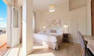 Et hotellrom med en dobbeltseng, nattbord, skrivebord og garderobe, samt en balkong med utsikt. (AI-generert tekst)