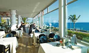 Restaurant med oppdekkede bord nær vinduer med havutsikt. (AI-generert tekst)