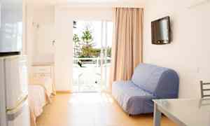 En lys stue med sofa, bord og en balkong med utsikt over trær. (AI-generert tekst)