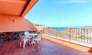 Terrasse med bord, stoler og rekkverk, samt havutsikt. (AI-generert tekst)