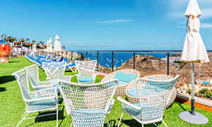 Hvite hagestoler på en plen med havet og landskap i bakgrunnen. (AI-generert tekst)