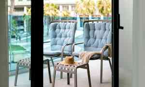 To blå stoler og en krakk med en hatt på en balkong. (AI-generert tekst)