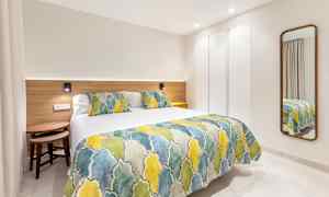 Et moderne hotellrom med en seng dekket med et fargerikt sengeteppe og puter, samt et speil på veggen. (AI-generert tekst)