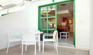 Uteplass med hvite møbler som vender mot en grønn innrammet dør med utsikt inn i en leilighet. (AI-generert tekst)