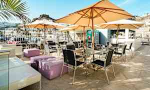 Utendørsterrasse med bord, stoler og parasoller, omgitt av fjellandskap. (AI-generert tekst)