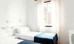 Et hotellrom med to enkeltsenger med hvite laken og blå tepper. (AI-generert tekst)