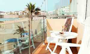 En balkong med utsikt over en strand og palmer, med bord og stoler. (AI-generert tekst)