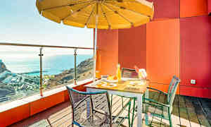 En terrasse med bord, stoler og parasoll med utsikt over havet. (AI-generert tekst)