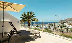 Terrasse med solsenger og parasoll, utsikt over småbåthavn og hav. (AI-generert tekst)