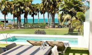 Utsikt over et basseng med solsenger ved siden av, hage med palmer og havet i bakgrunnen. (AI-generert tekst)