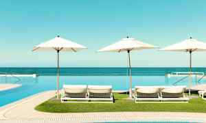 Utsikt over solsenger med parasoller ved et infinitybasseng, havet i bakgrunnen. (AI-generert tekst)