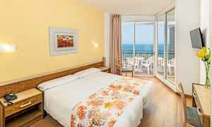 Hotellrom med to senger, gult interiør og en balkong med utsikt over havet. (AI-generert tekst)