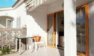 Terrasse med hvit bygning, bord og stol, samt en dør som fører inn i huset. (AI-generert tekst)