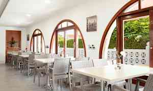 Restaurant med bueformede vinduer og bord med stoler. Planter utenfor vises gjennom vinduene. (AI-generert tekst)