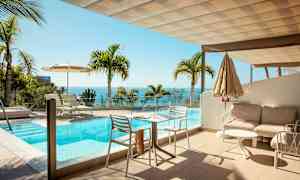 En terrasse med et basseng og utsikt over havet, omgitt av palmer. (AI-generert tekst)