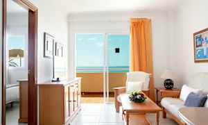 En stue med sofa, bord og utsikt over havet fra en glassdør. (AI-generert tekst)