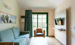 En stue med en blå sofa, rottingstol og en TV montert på veggen. (AI-generert tekst)