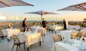 Utendørs servering med dekkede bord og parasoller, med utsikt over sanddyner i bakgrunnen. (AI-generert tekst)