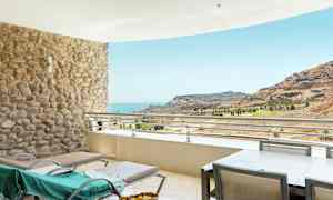 Terrasse med solsenger og utsikt over havet og et fjellandskap. (AI-generert tekst)