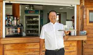 En person holder et brett med to glass foran en serveringsdisk i tre. (AI-generert tekst)