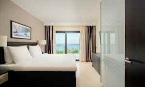 Hotellrom med en dobbeltseng, vindu med havutsikt. (AI-generert tekst)