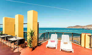 En terrasse med utsikt over havet, utstyrt med solsenger, bord og stoler. (AI-generert tekst)