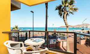 Utsikt fra en balkong med bord og stoler mot havet og stranden. (AI-generert tekst)