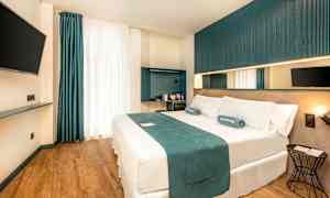 Et moderne hotellrom med en dobbeltseng, veggmontert TV og minimalistisk interiør. (AI-generert tekst)