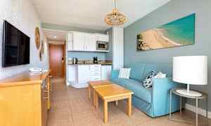 Leilighetsrom med blå sofa, tremøbler og kjøkkenområde. (AI-generert tekst)