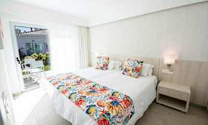 Et hotellrom med to enkeltsenger, fargerike putetrekk og en dør til en terrasse. (AI-generert tekst)