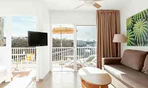 Interiør av et lyst hotellrom med balkong, utsikt over en dal. (AI-generert tekst)