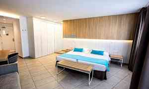 Et moderne hotellrom med en dobbeltseng, en trebenk ved fotenden og et skrivebord i hjørnet. (AI-generert tekst)