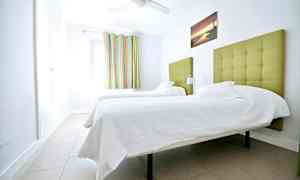 Et rom med to enkeltsenger med grønn polstret sengegavl. (AI-generert tekst)