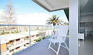 En balkong med hvite stoler og utsikt over bygninger og palmer. (AI-generert tekst)