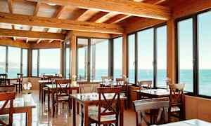 En kafé med trebord og stoler, med store vinduer som viser utsikt mot havet. (AI-generert tekst)