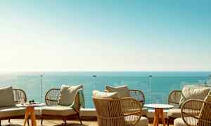 Loungeområde med sittemøbler, et glassrekkverk og utsikt over havet. (AI-generert tekst)