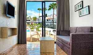 Utsikt over en stue med sofa og bord samt en åpning til en balkong med utsikt over et basseng. (AI-generert tekst)