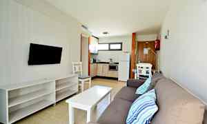 En moderne hotellromsleilighet med sofa, TV, bord og kjøkken. (AI-generert tekst)