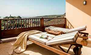 To solsenger med stripete puter står på en terrasse med utsikt over frodige åser. (AI-generert tekst)