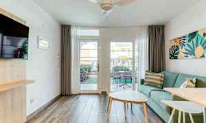 Et lyst oppholdsrom med en grønn sofa, et salongbord og utsikt mot en terrasse gjennom et glassvindu. (AI-generert tekst)