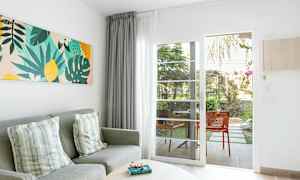 Stuemiljø med grå sofa, puter, fargerik veggkunst og glassdør som leder til uteplass. (AI-generert tekst)