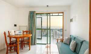 Et rom med spisebord og stoler, sofa og glassdør til en balkong. (AI-generert tekst)