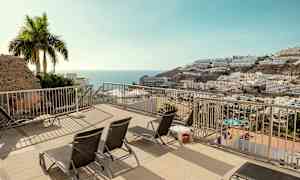 En terrasse med solsenger og utsikt over havet og bygninger på en skråning. (AI-generert tekst)