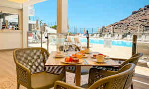 Et bord med frokost og stoler foran et basseng med fjell i bakgrunnen. (AI-generert tekst)