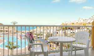 Utsikt fra en balkong med hvite møbler mot et basseng og havutsikt. (AI-generert tekst)