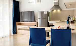 Et kjøkken med en benk, to blå stoler, et kjøleskap og en TV ved et treskap. (AI-generert tekst)