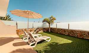 En uteplass med to solsenger, parasoll og kunstgress. (AI-generert tekst)